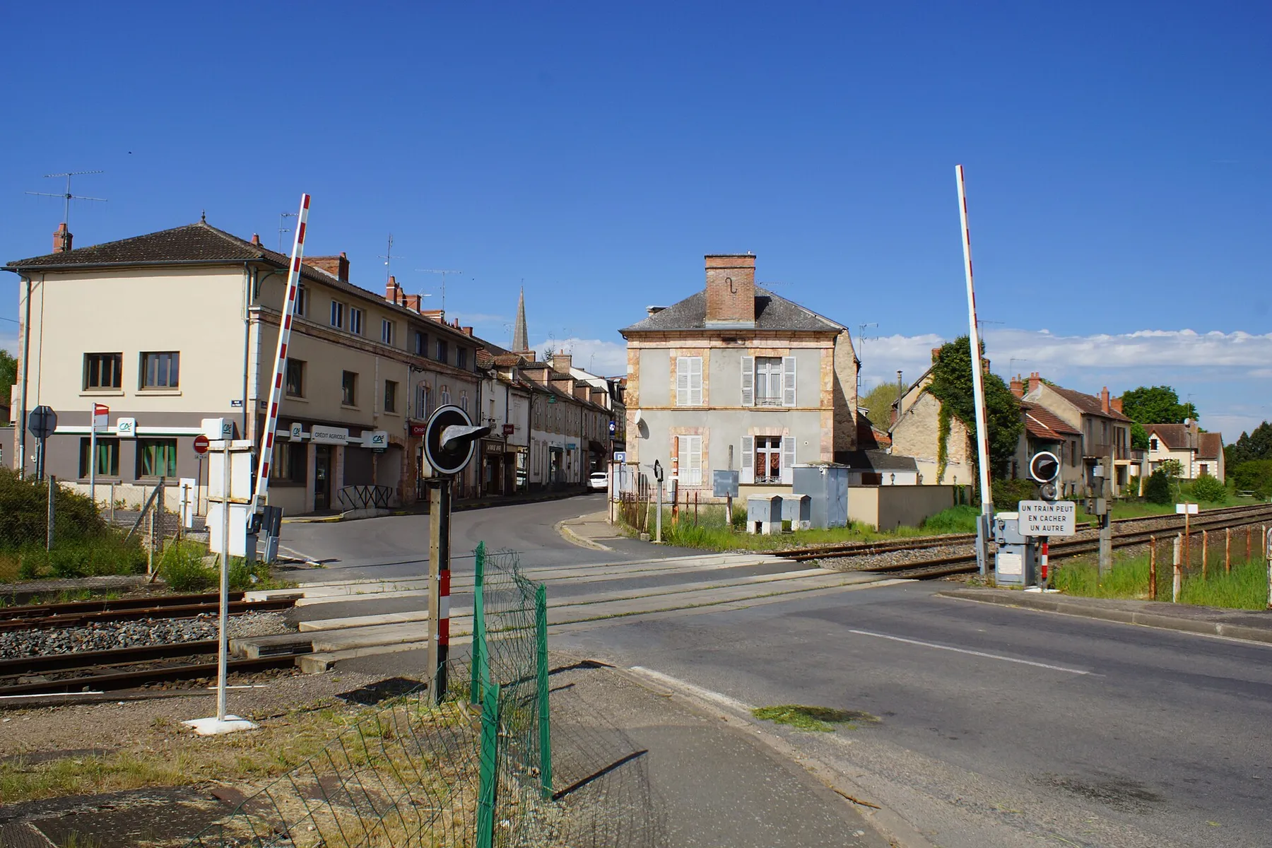 Passage à niveau à proximité de la gare qui se trouve à gauche.